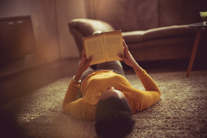 I read to feed my curiosities. African American woman reading book at home.