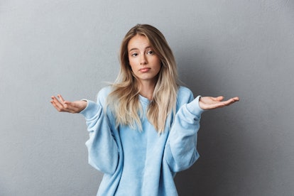 Portrait of a frustrated young blonde girl shrugging shoulders isolated over gray background