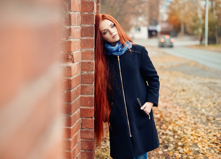 Woman with long red hair walks in autumn on the street. Mysterious dreamy look and the image of the ...