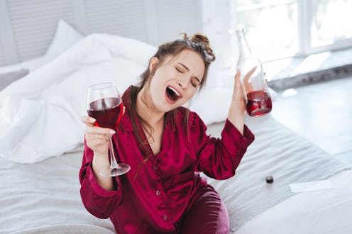 Songs and wine. Dark-haired woman with messy hair singing songs while drinking wine on her own