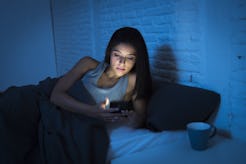 young beautiful womanl in bed using mobile phone late at night at dark bedroom lying happy and relax...