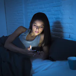 young beautiful womanl in bed using mobile phone late at night at dark bedroom lying happy and relax...