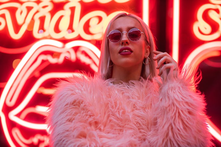 Woman standing in front of bright neon sign, thinking about how November 15, 2021 will be the best w...