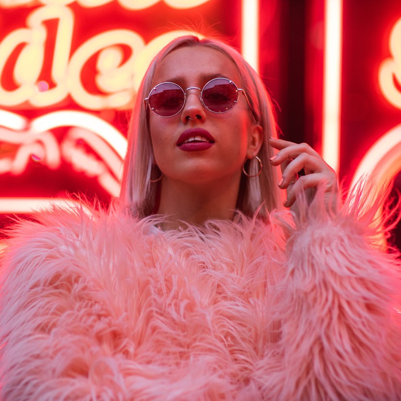 Woman standing in front of bright neon sign, thinking about how November 15, 2021 will be the best w...
