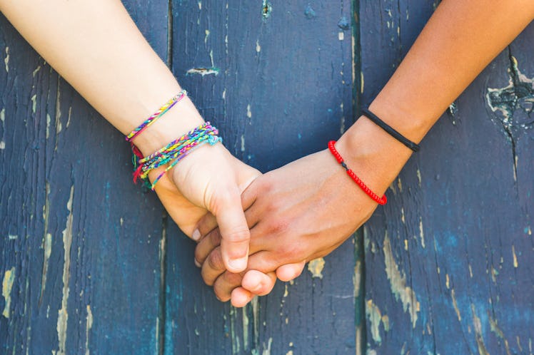 Two women holding hands with a wooden background. One is caucasian, the other is black. Multicultura...