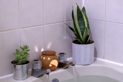 Interior - bathroom, focussing on corner and foot of bath, with plants and candle, essential oil bur...