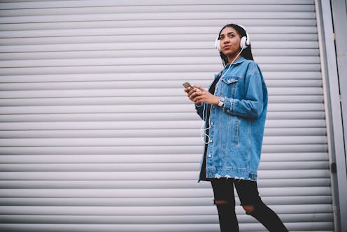 Dreamy afro american lover of music dressed in stylish casual denim jacket enjoying songs from playe...