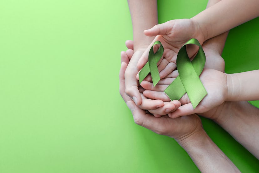 Adult and child hands holding Lime Green Ribbon on green background, children Mental health awarenes...