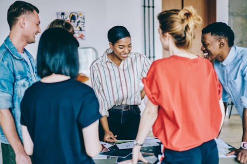 Group of young multicultural people in casual wear laughing during colaboration on design project in...