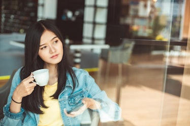 Asian woman with beautiful smile hold mobile phone during rest in coffee shop.Attractive woman drink...