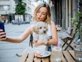 A blonde woman takes a picture with her dog while eating at a dog-friendly brunch spot in NYC.