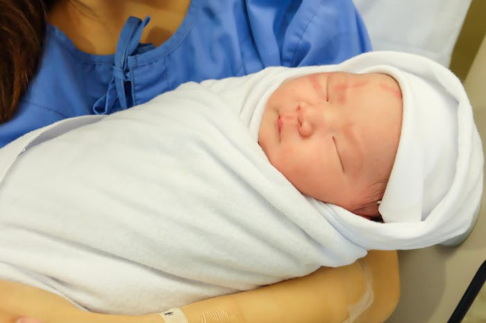 Newborn baby sleeps swaddled in a white blanket in mother's arms