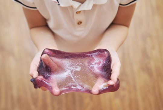 Kid holds glitter purple  slime in hands.