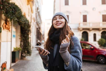 Cheerful cute young woman using cell phone and eating ice cream in the city