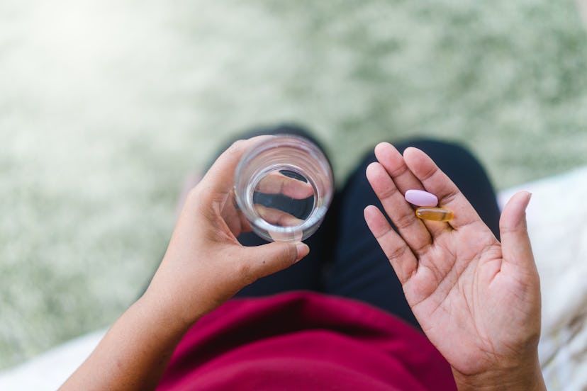 Close Up Of Senior woman holding Calcium supplement tablet pills and Omega 3 oil with glass of water...