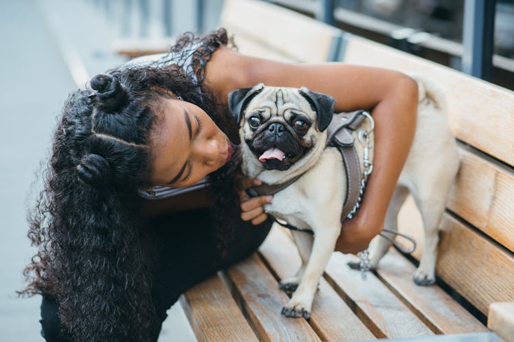 A woman kisses her pug while sitting on a park bench in the city during the holidays.