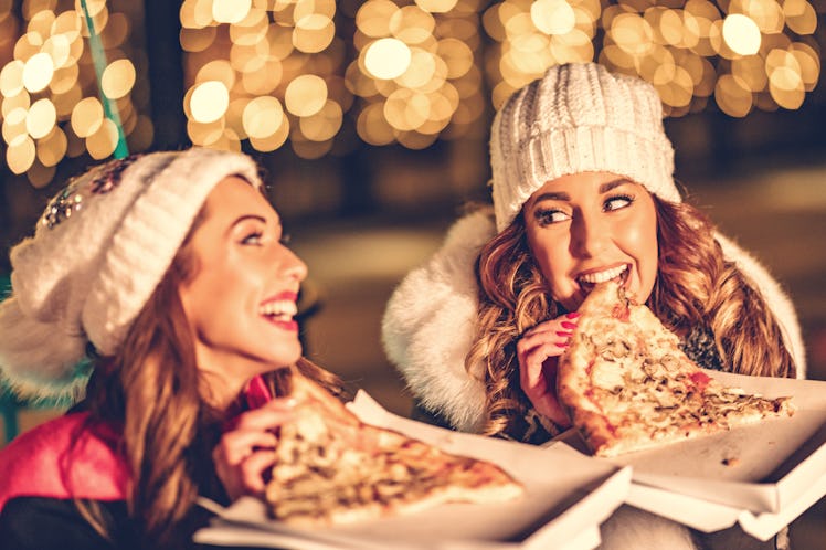 Two women enjoy date night outside and laugh with slices of pizza in their hands.