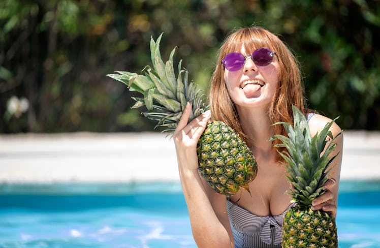Caucasian girl with sunglasses holding two pineapples in a pool