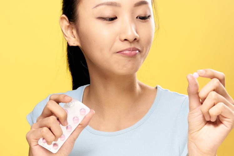 Asian woman on a yellow background holds a pill.