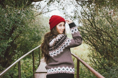 A girl in red hat and knitted sweater walks down a boardwalk in a park. 