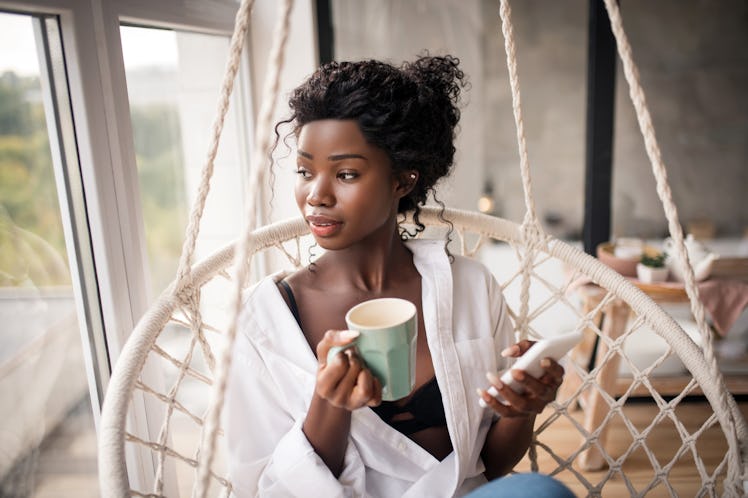 Looking into window. Curly dark-skinned woman looking into window while enjoying coffee