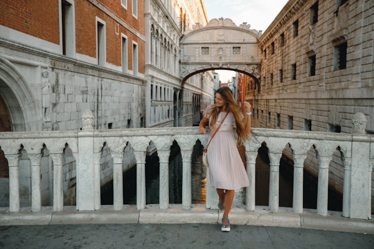 A girl poses in front of a bridge in a pink dress in Venice, Italy during a trip.