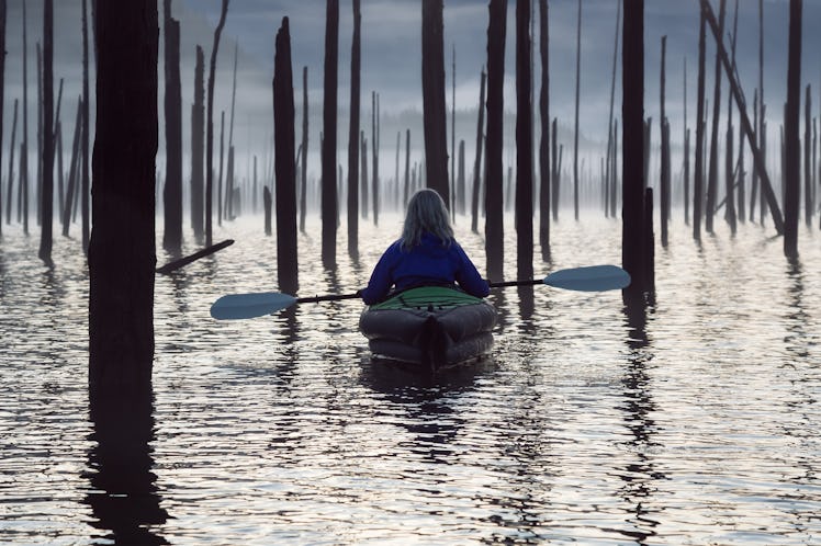 Adventurous Girl kayaking on an infatable kayak in a beautiful lake during a calm and peaceful sunri...