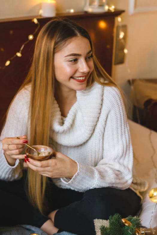 A blonde girl smiles and looks to the side while sitting on a couch and eating ice cream.