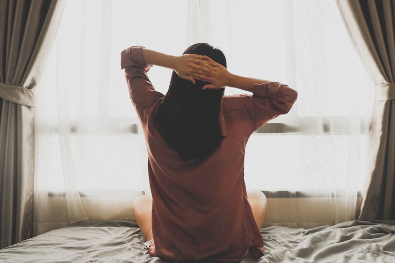 Not fully focused back view image of a woman stretching in bed after waking up