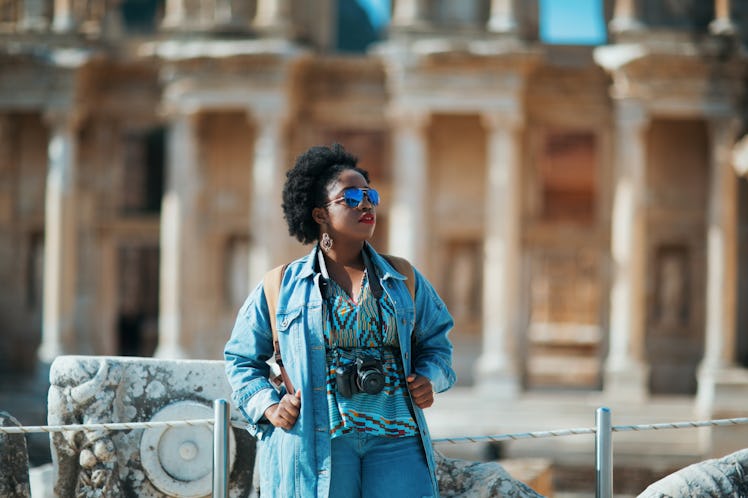 A woman dressed in denim admires a city while holding a camera around her neck.