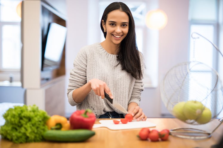 The young woman cuts vegetables in the kitchen with a knife and laptop on the table. Vegetable Salad...