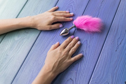 Anal plug with a fluffy pink tail with female hands. Toy for adult games.