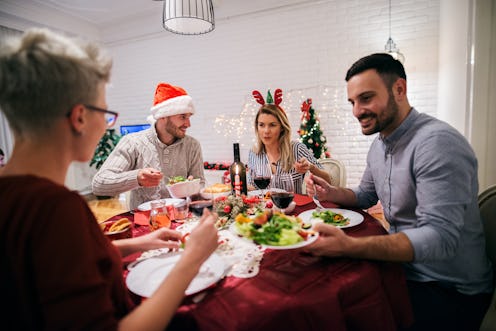 Two young couples having christmas dinner together. Sitting at decorated table full of food and havi...