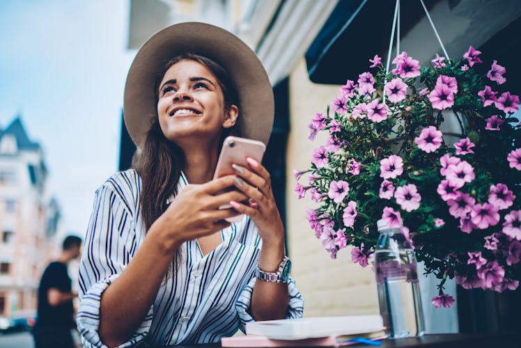 Cheerful dreamy stylish student wearing cool hat and looking up while received notification with goo...