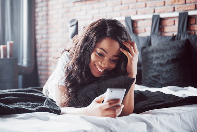 Portrait of beautiful woman waking up in her bed and looks into the phone. Check social networks, se...