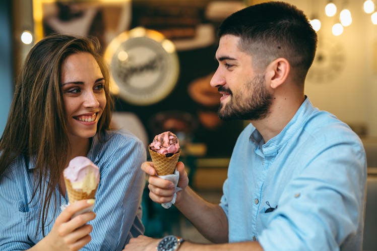 A couple laughs and smiles at each other in an ice cream parlor holding up cones of gingerbread ice ...