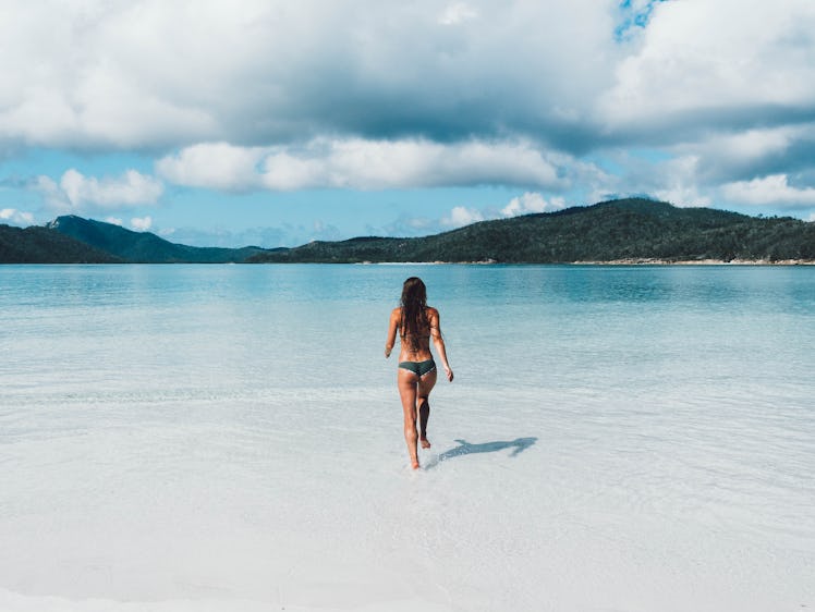 A woman runs into the ocean water on a beach in Australia.