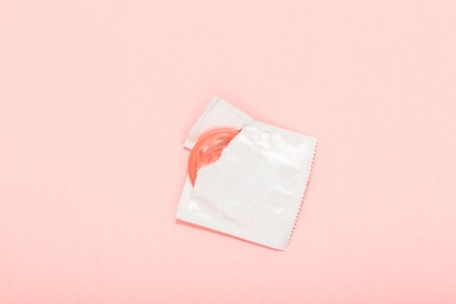 Pink opened condom and condom in pack on a pink background. Using a condom can reduce the probabilit...