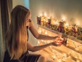 A blonde woman sets up little holiday gift boxes and string lights on shelves in her home.