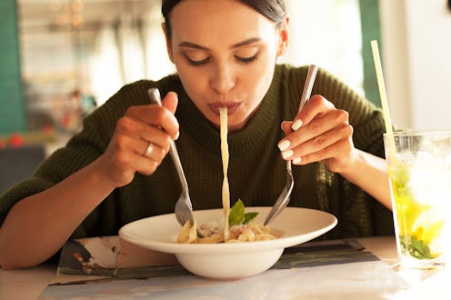 young beautiful woman eating pasta in restourant or cafe and drink mojito. female wearing green swea...