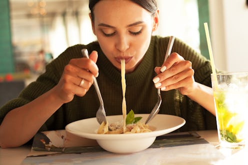 young beautiful woman eating pasta in restourant or cafe and drink mojito. female wearing green swea...