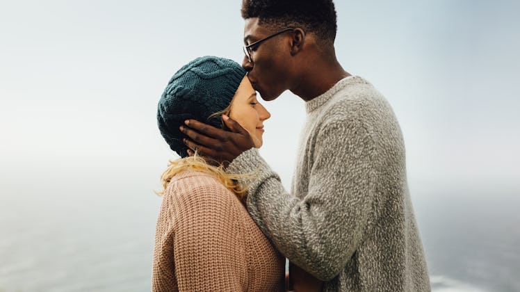 Side view of loving interracial couple together outdoors. Young man kissing forehead of his girlfrie...