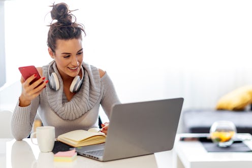 Woman with headphones over her neck sitting on the desk with note book, laptop and work