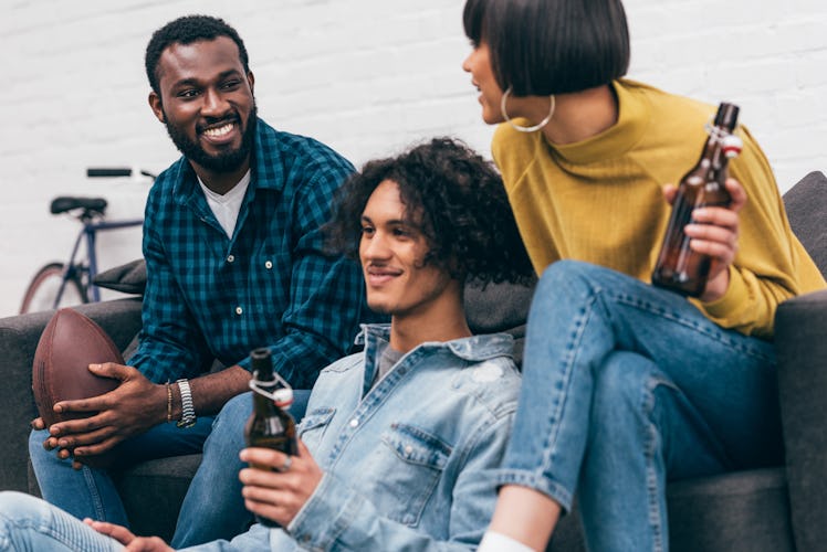 A group of three friends relax on a couch while one holds a football.