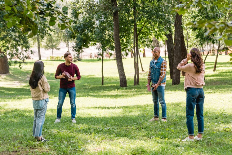 A group of four friends playing football in the park on a sunny day.