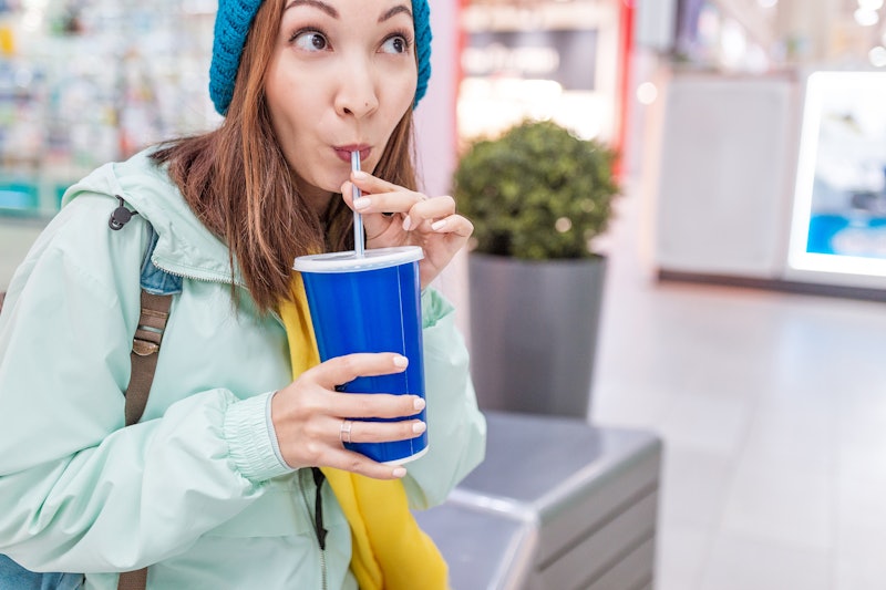 happy woman drinking soda with straw in a mall