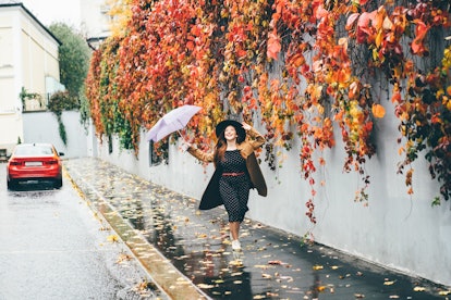 Young happy emotional girl laughing and jumping with umbrella on colored autumn street. Woman with u...