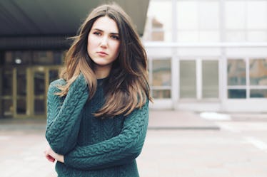 Young woman wearing woolen green sweater walking in the winter city street. Warm soft cozy image. Co...