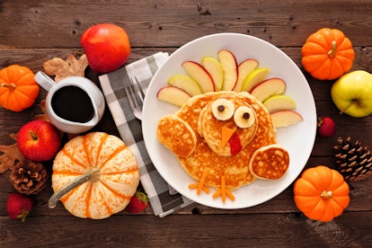 A Thanksgiving breakfast table is set with turkey-shaped pancakes, apples, pinecones, and little pum...