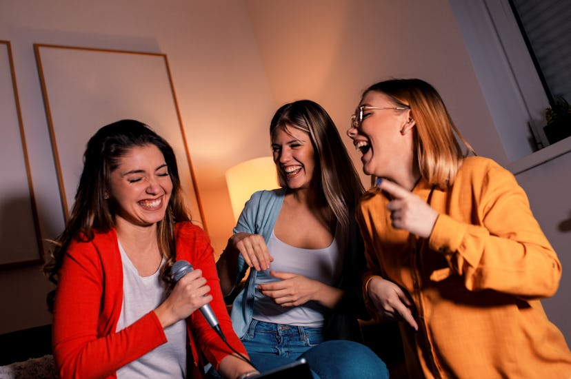 Three female friends having fun playing karaoke at home.